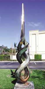 Abstract sculpture of a flame in a grass area near a parking lot